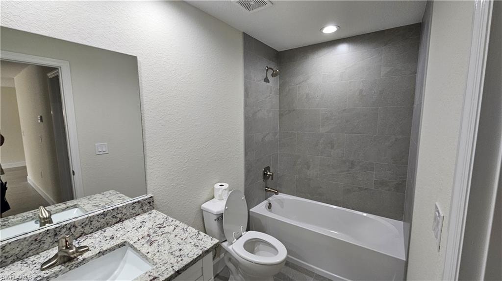 Full bath featuring toilet, shower / tub combination, vanity, and a textured wall