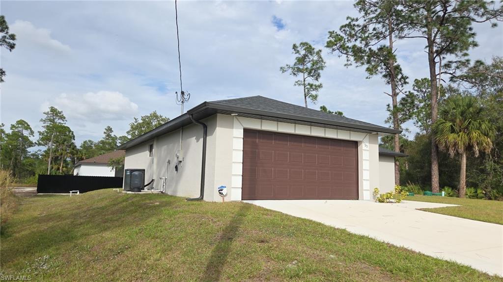 View of side of home featuring stucco siding, a lawn, a shingled roof, and driveway