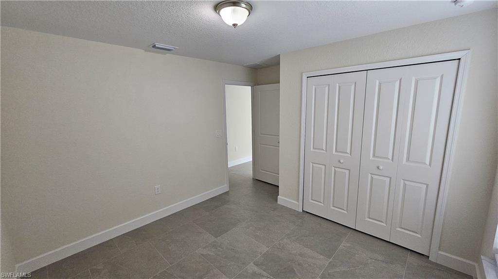 Unfurnished bedroom featuring a textured ceiling, a closet, and baseboards