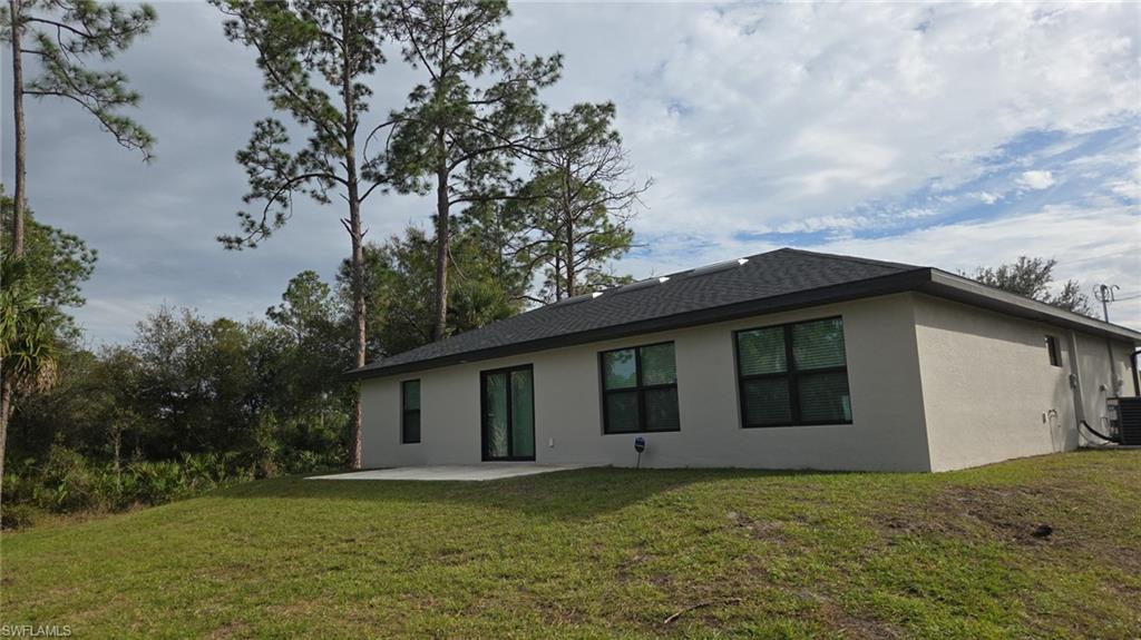 Back of house with stucco siding, a patio, a yard, and a shingled roof