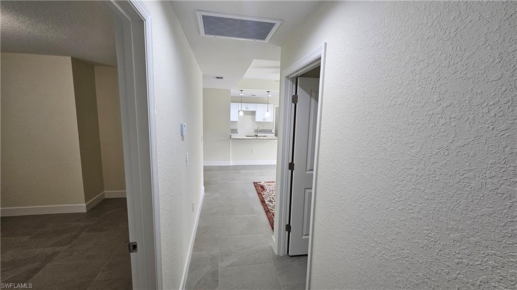 Hallway with a textured wall, tile patterned floors, and baseboards