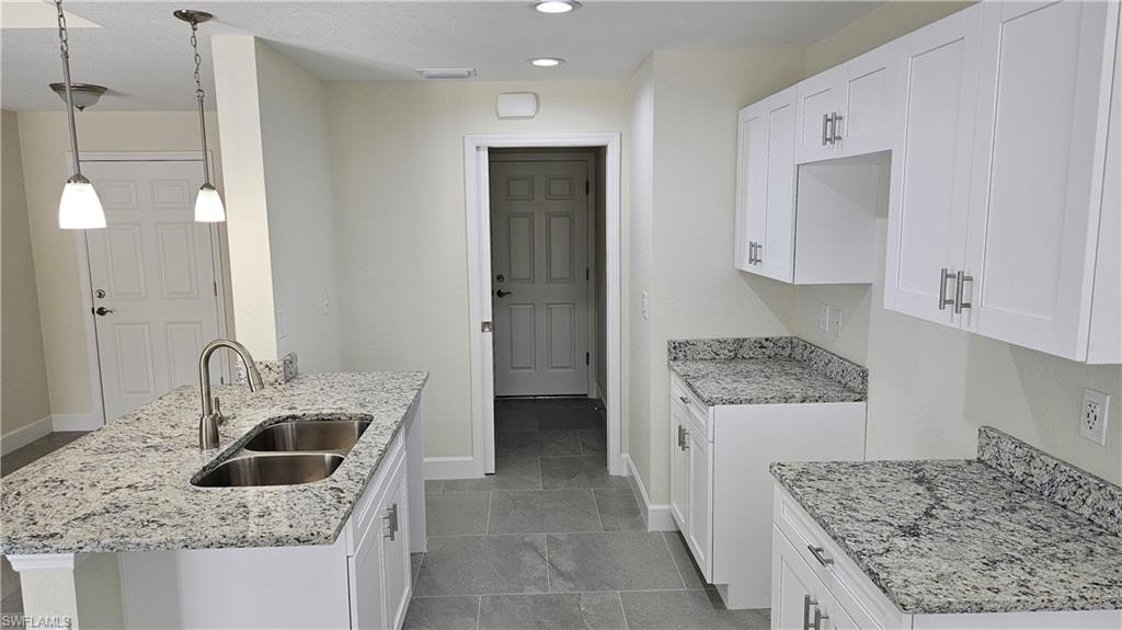 Kitchen with a sink, baseboards, light stone countertops, recessed lighting, and white cabinets