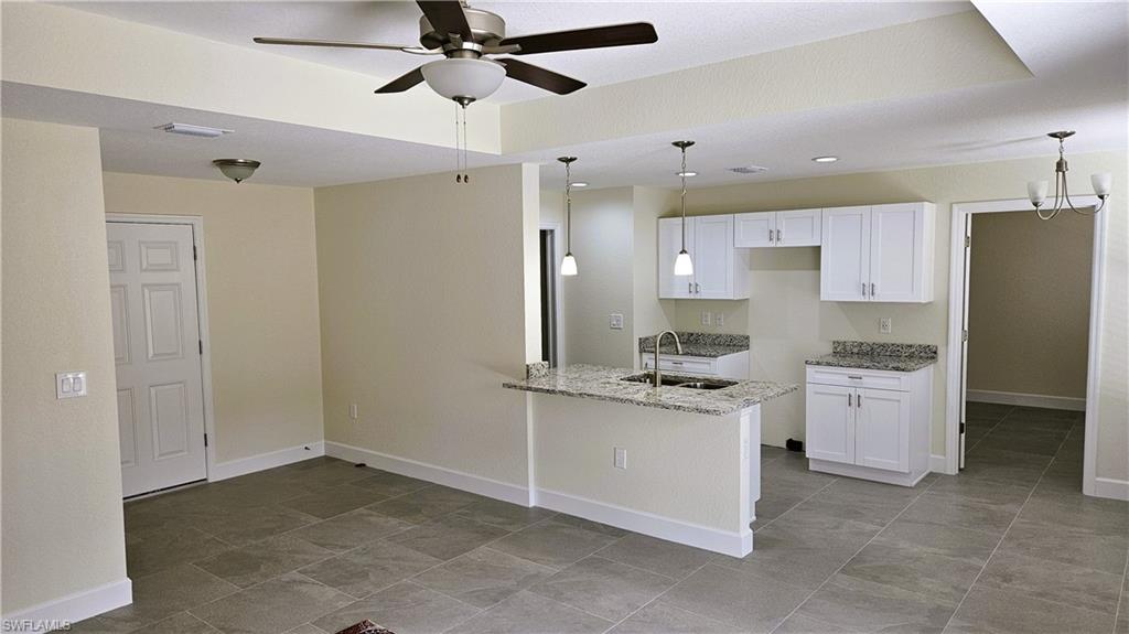 Kitchen with a sink, light stone countertops, white cabinets, a ceiling fan, and a peninsula