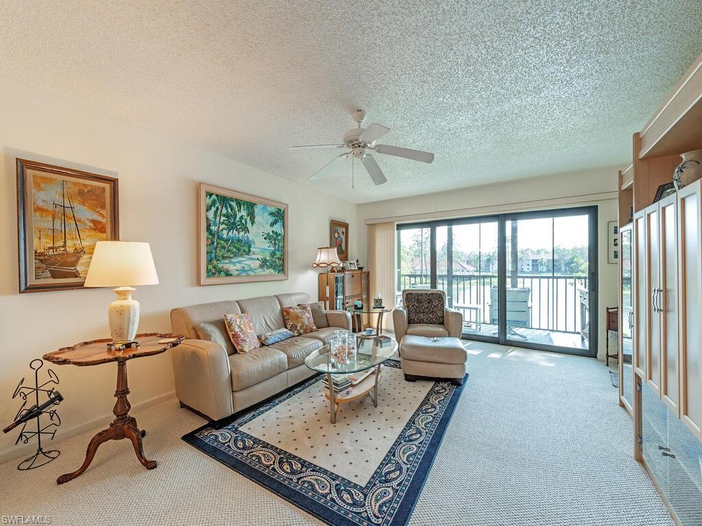 Carpeted living room featuring ceiling fan, baseboards, and a textured ceiling