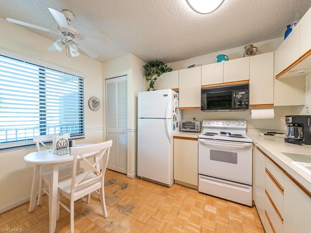 Kitchen with white appliances, light countertops, a textured ceiling, and white cabinets