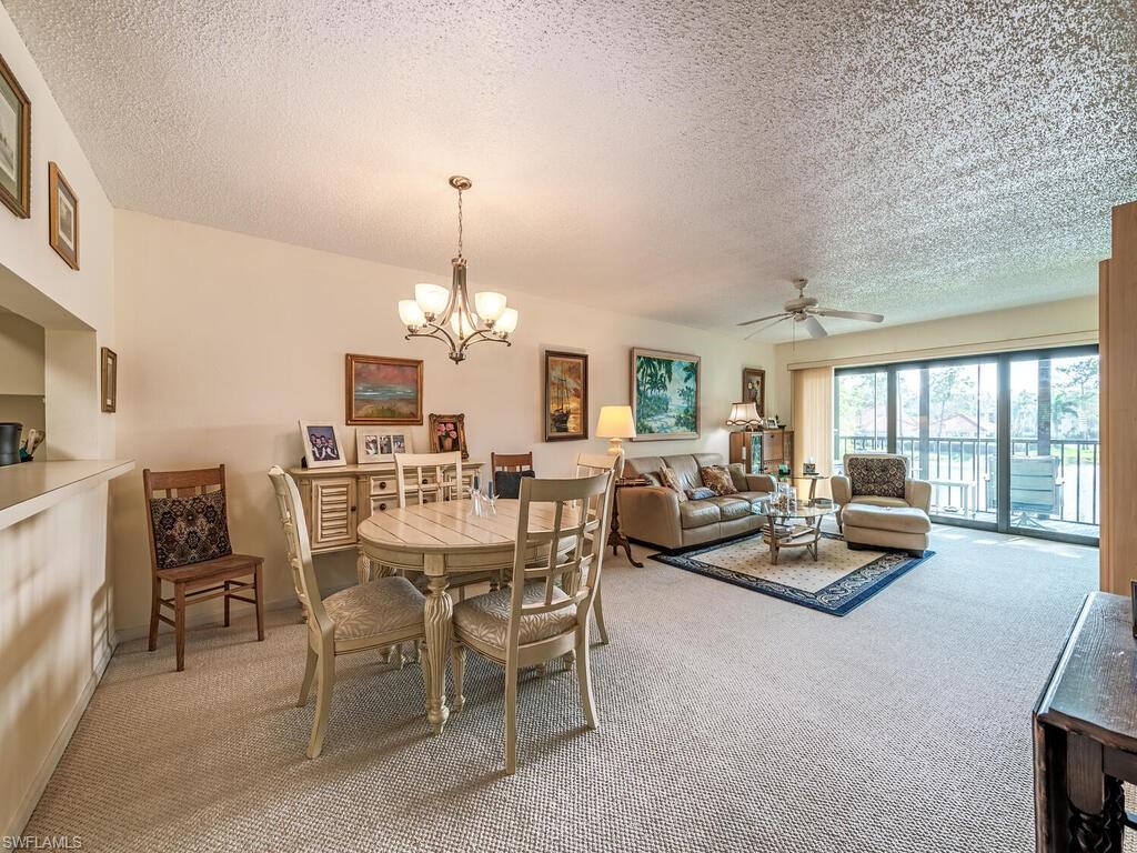 Carpeted dining area featuring baseboards, a textured ceiling, and ceiling fan with notable chandelier