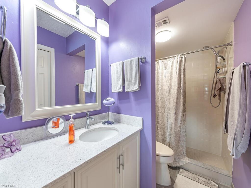 Bathroom with toilet, vanity, visible vents, and a shower stall