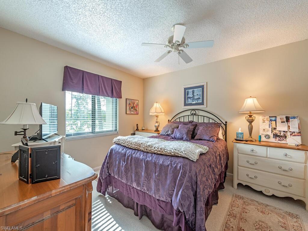 Bedroom with a ceiling fan, light carpet, and a textured ceiling