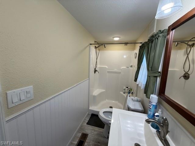 Bathroom with a textured ceiling, a textured wall, a wainscoted wall, a sink, and a shower stall