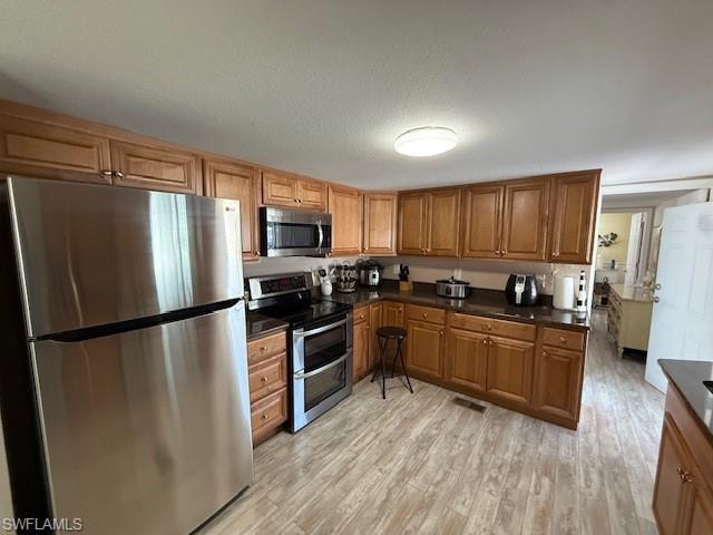 Kitchen with dark countertops, brown cabinetry, and stainless steel appliances