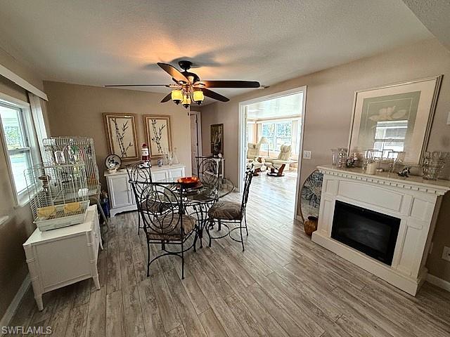 Dining area featuring baseboards, a glass covered fireplace, ceiling fan, wood finished floors, and a textured ceiling