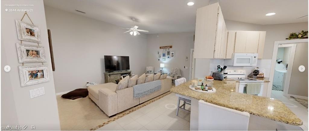 Kitchen with a kitchen breakfast bar, white appliances, open floor plan, light stone countertops, and a ceiling fan