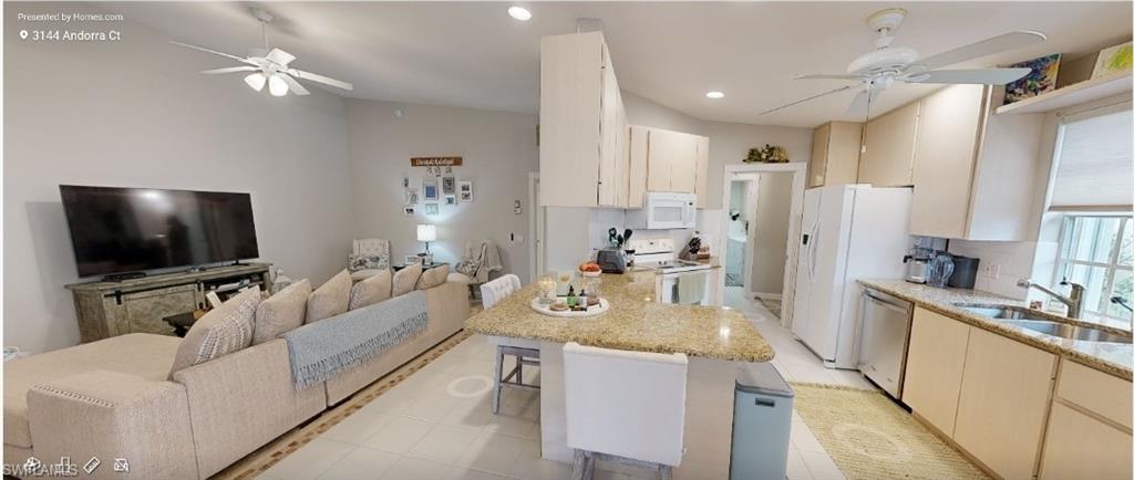 Kitchen featuring ceiling fan, open floor plan, white appliances, a breakfast bar, and a peninsula