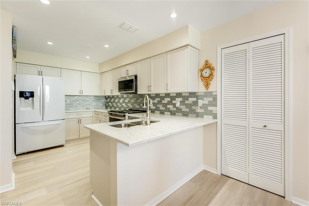 Kitchen with light wood-style flooring, stainless steel appliances, a peninsula, a sink, and decorative backsplash
