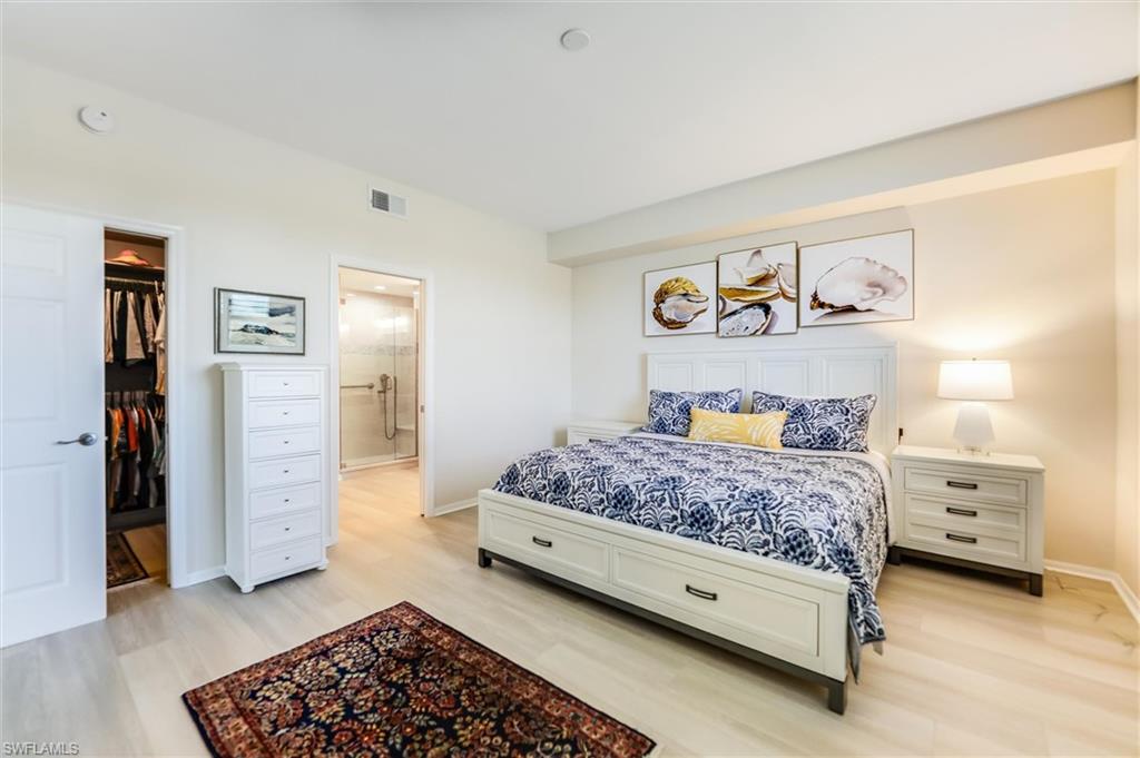 Bedroom featuring a walk in closet, visible vents, light wood-style flooring, ensuite bathroom, and baseboards