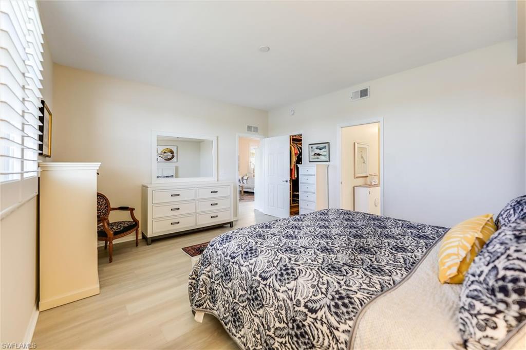 Bedroom with light wood-style floors, visible vents, baseboards, and ensuite bathroom