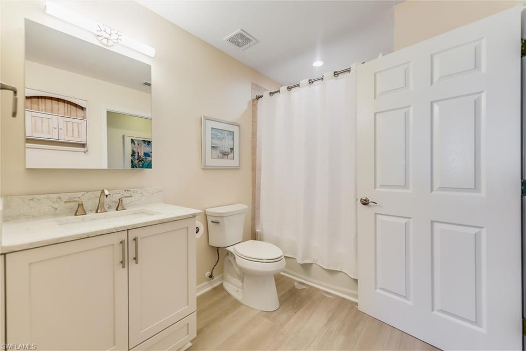 Bathroom with shower / bath combination with curtain, visible vents, toilet, vanity, and wood finished floors