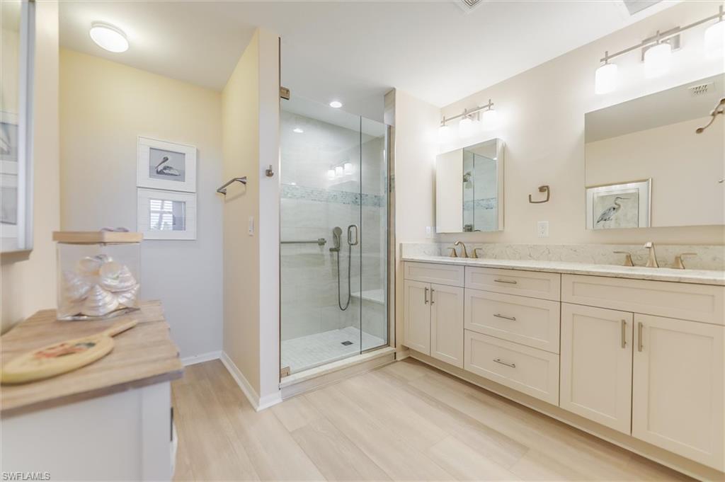 Full bathroom with a stall shower, double vanity, a sink, and wood finished floors