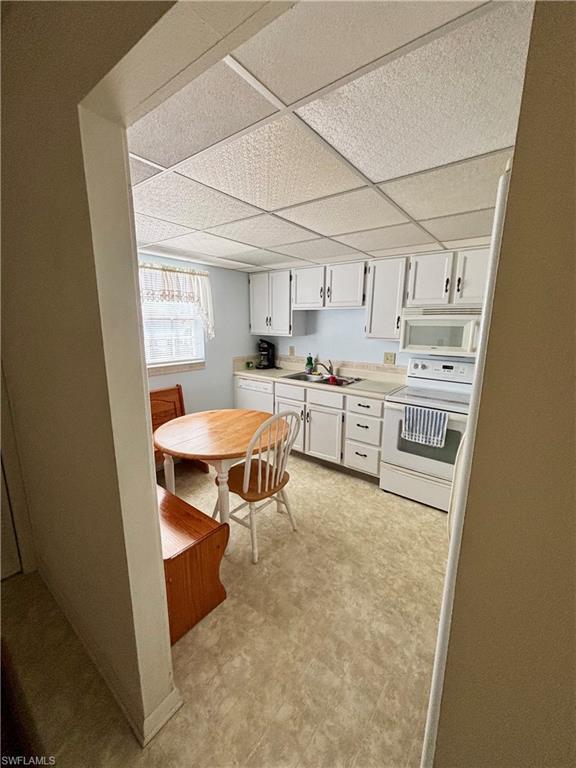 Kitchen with white appliances, light countertops, light floors, white cabinetry, and a sink
