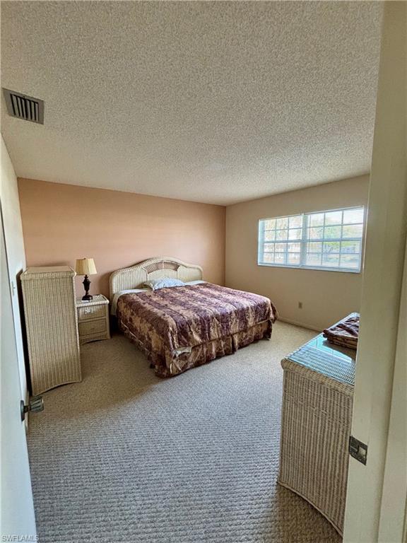 Bedroom with a textured ceiling, carpet flooring, and visible vents