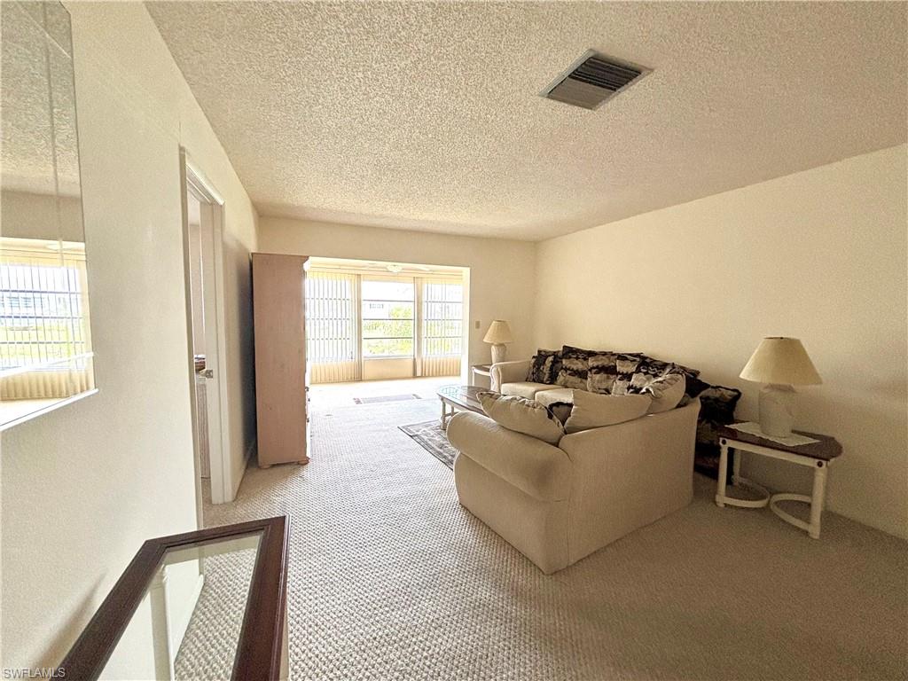 Living area with carpet floors, visible vents, and a textured ceiling