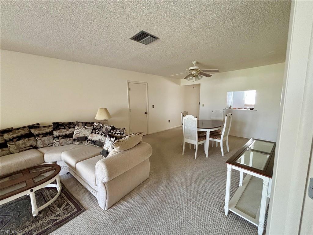 Carpeted living area with ceiling fan, a textured ceiling, and visible vents