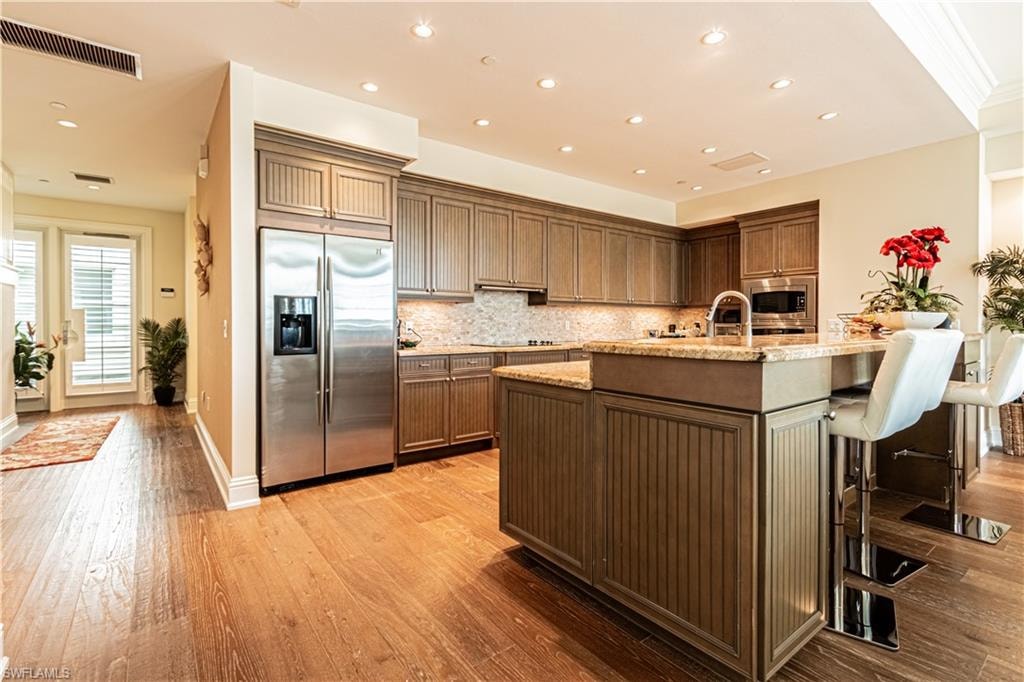Kitchen featuring light stone counters, light wood-style flooring, visible vents, appliances with stainless steel finishes, and decorative backsplash