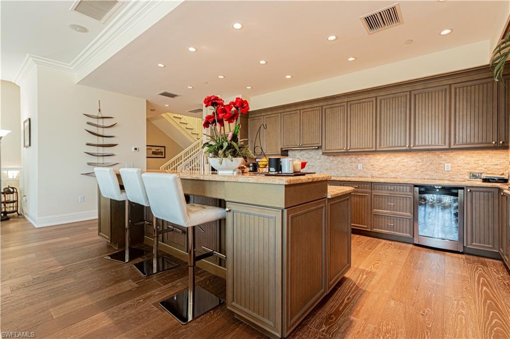 Kitchen featuring light wood finished floors, a center island with sink, visible vents, and a kitchen breakfast bar