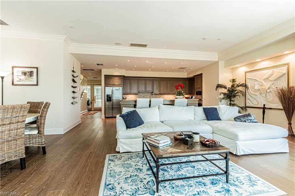 Living area featuring baseboards, visible vents, dark wood finished floors, and ornamental molding