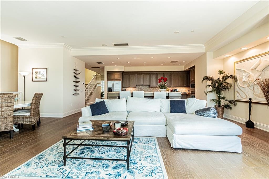 Living room featuring visible vents, ornamental molding, wood finished floors, baseboards, and stairs