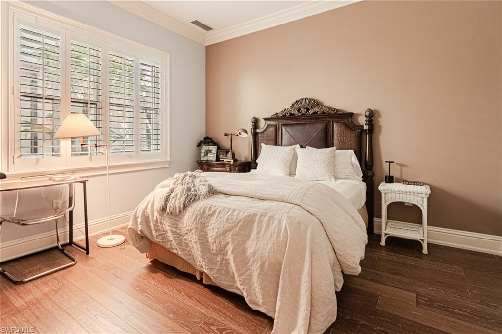 Bedroom with baseboards, wood finished floors, visible vents, and crown molding