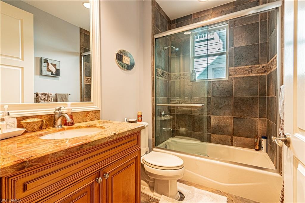 Full bathroom featuring shower / bath combination with glass door, vanity, and toilet