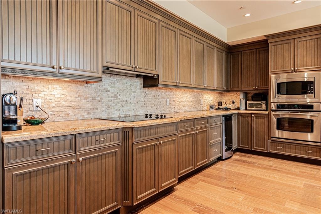 Kitchen with stainless steel appliances, backsplash, light wood-style floors, ventilation hood, and beverage cooler