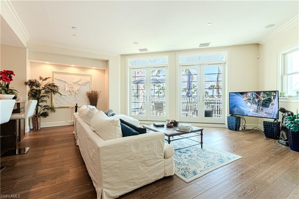 Living room with baseboards, wood finished floors, visible vents, and crown molding