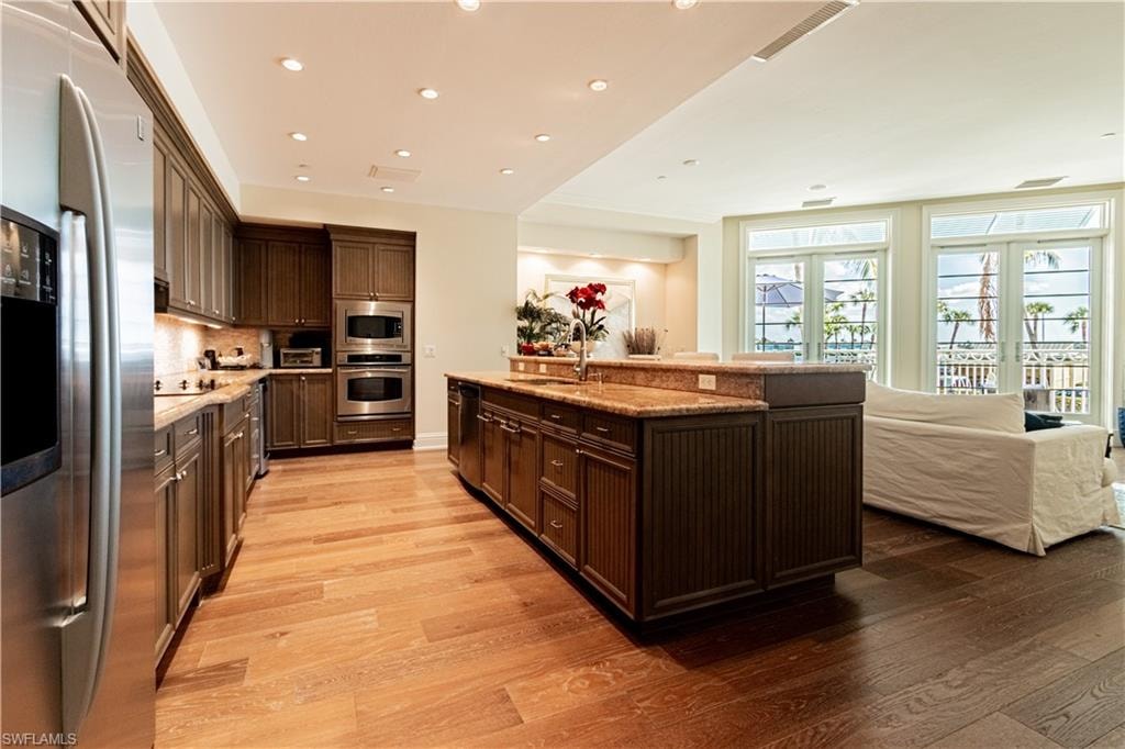 Kitchen featuring light wood-style flooring, dark brown cabinets, french doors, appliances with stainless steel finishes, and decorative backsplash
