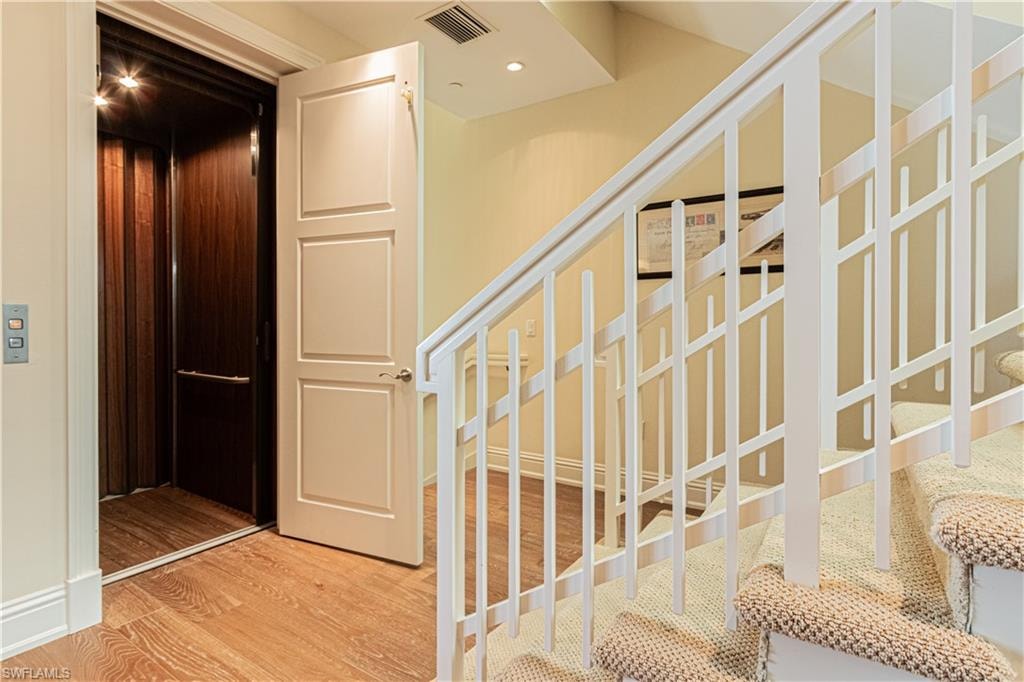 Stairway with recessed lighting, wood finished floors, visible vents, and elevator
