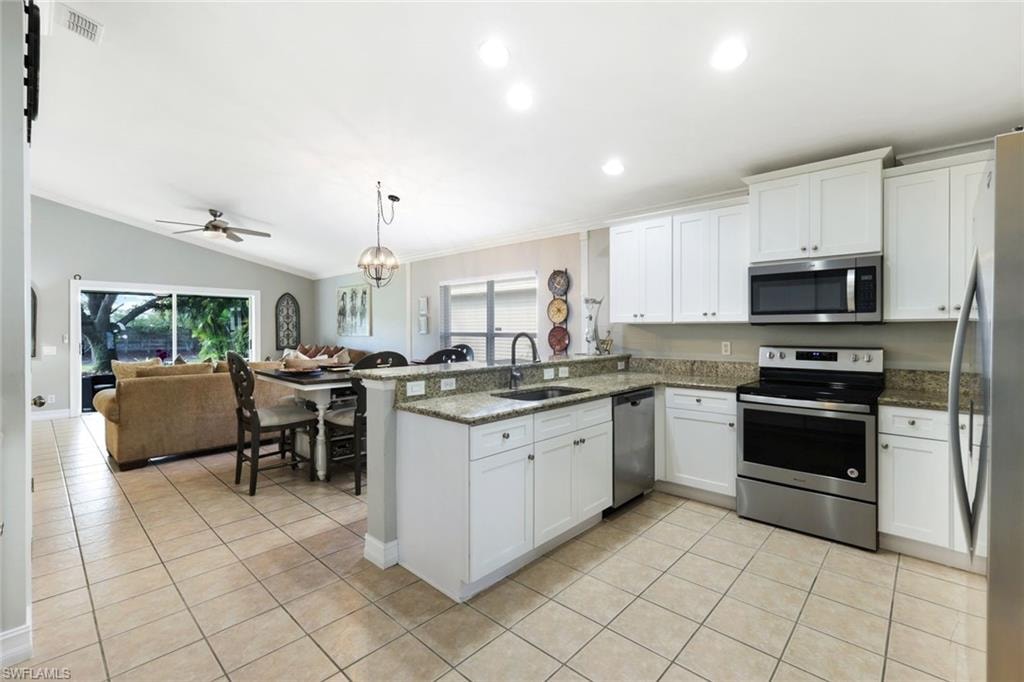Kitchen with light tile patterned floors, appliances with stainless steel finishes, open floor plan, a peninsula, and a sink