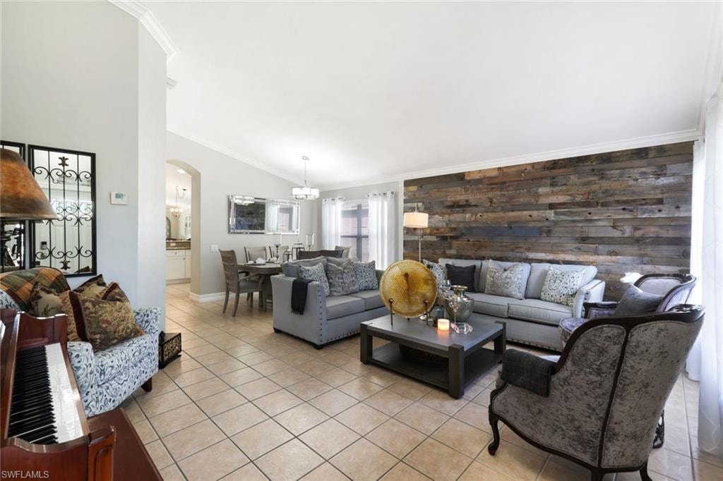 Living room with light tile patterned floors, arched walkways, an accent wall, vaulted ceiling, and crown molding