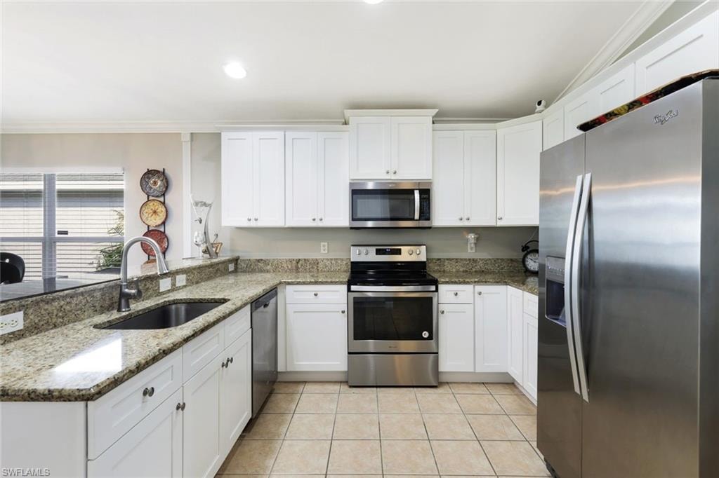 Kitchen with appliances with stainless steel finishes, white cabinets, a sink, and light tile patterned flooring