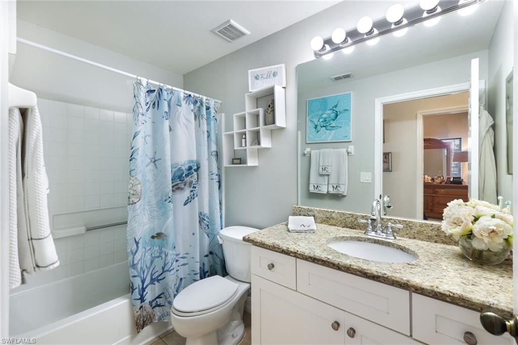 Bathroom featuring toilet, shower / tub combo, vanity, and visible vents