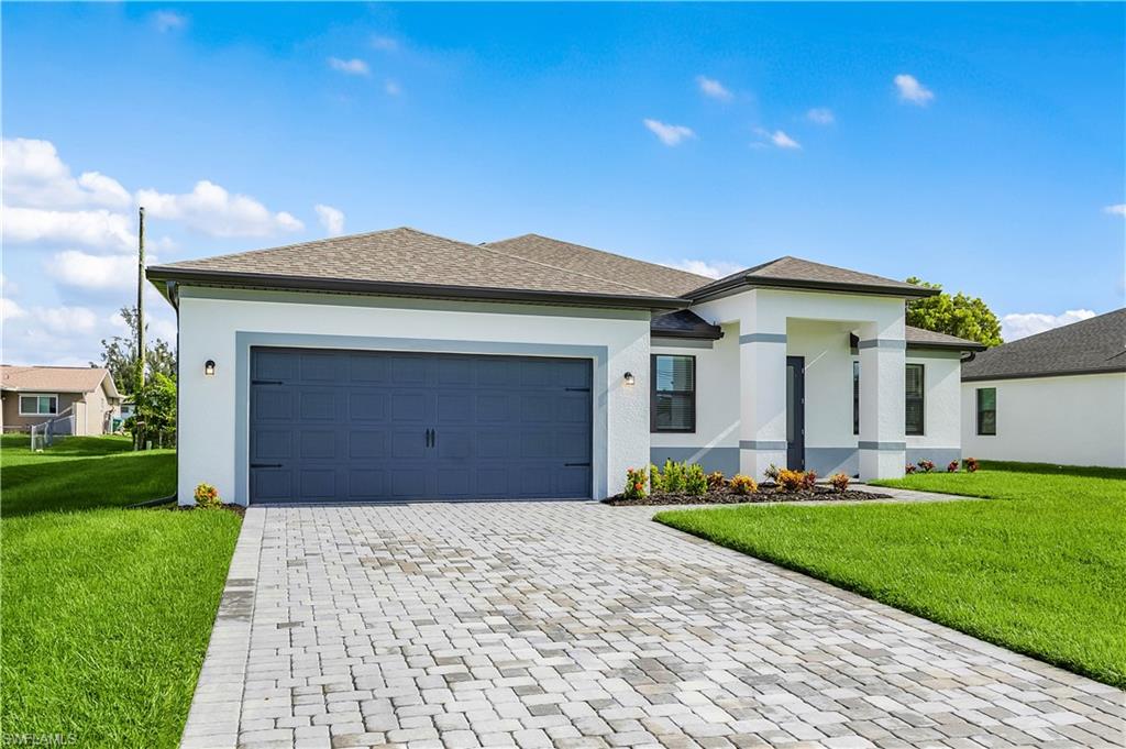 Prairie-style home with a front yard, decorative driveway, stucco siding, and a garage