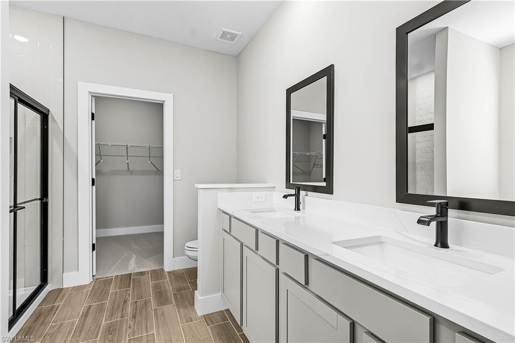 Bathroom with a walk in closet, double vanity, wood tiled floors, and a shower with shower door
