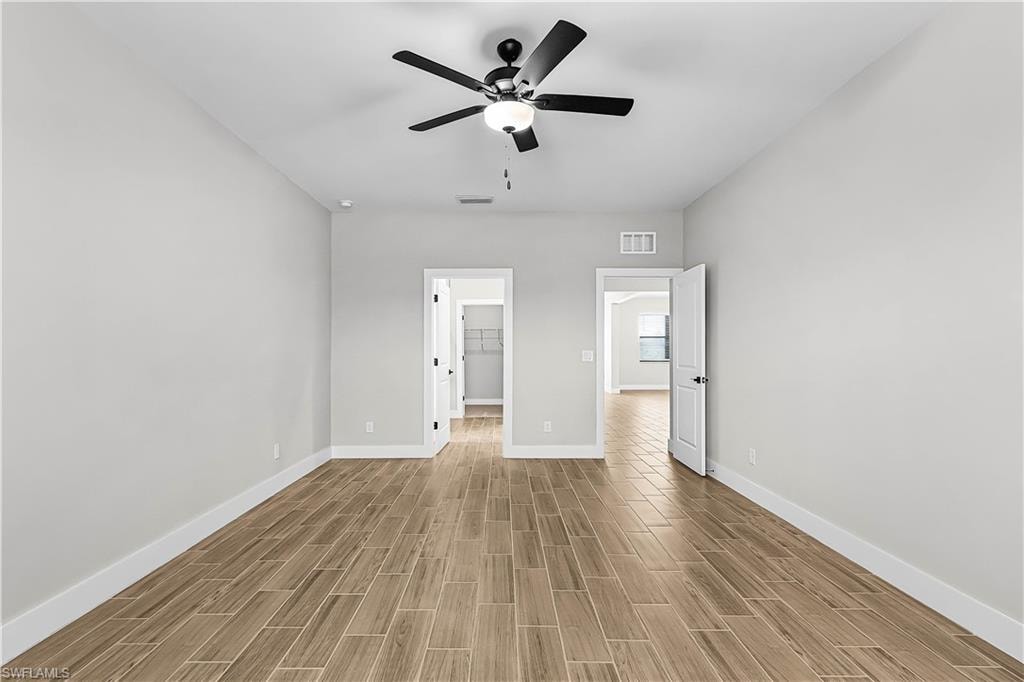 Unfurnished bedroom featuring a spacious closet, wood finish floors, and a ceiling fan