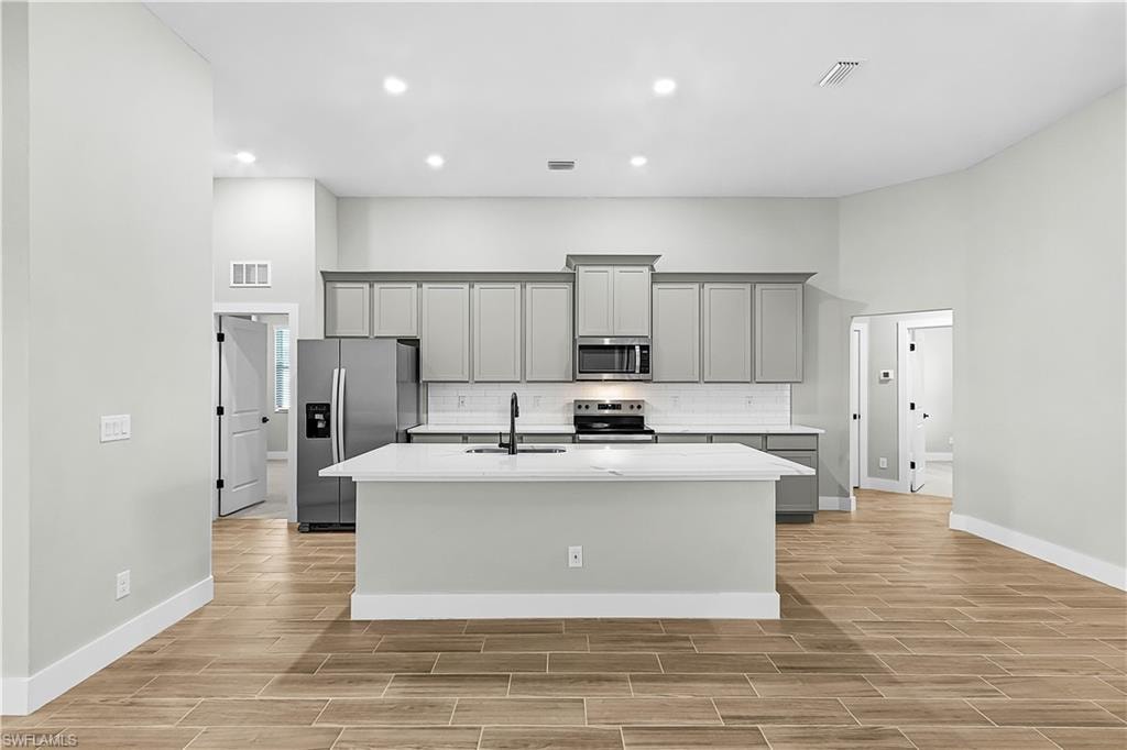 Kitchen featuring stainless steel appliances, gray cabinets, tasteful backsplash, wood tiled floors, and a center island with sink