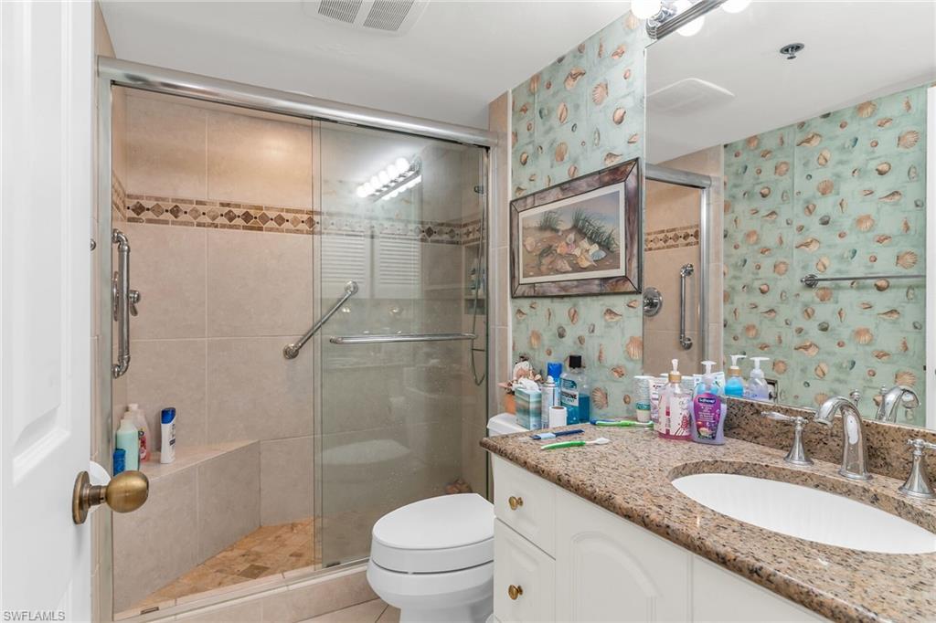 Bathroom featuring toilet, vanity, visible vents, a stall shower, and wallpapered walls