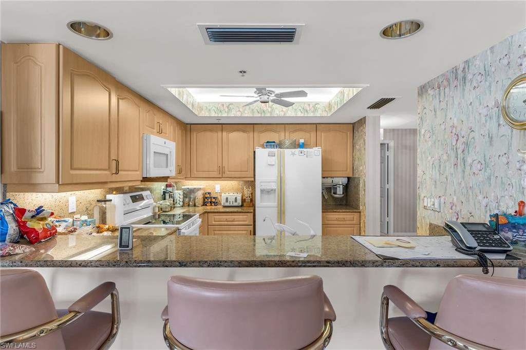 Kitchen with a peninsula, white appliances, and visible vents