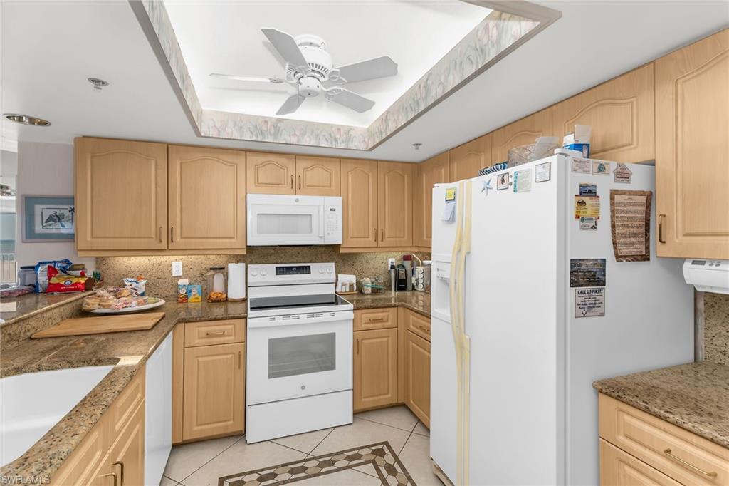 Kitchen featuring white appliances, light tile patterned floors, a tray ceiling, and light brown cabinetry