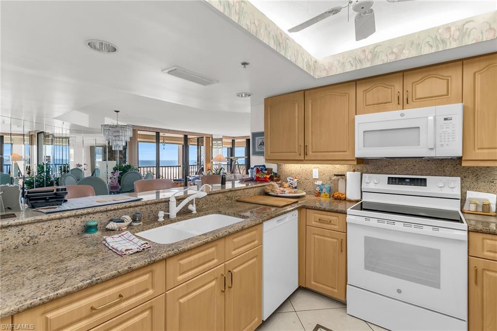 Kitchen with white appliances, light tile patterned flooring, a sink, and light stone counters