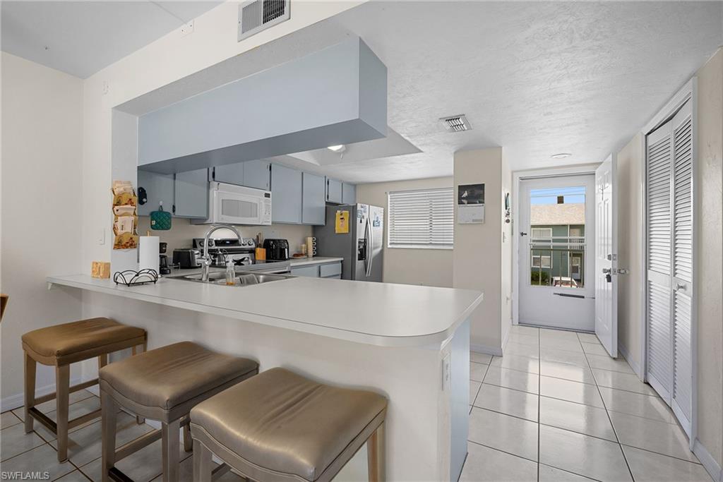 Kitchen featuring a peninsula, light countertops, light tile patterned floors, a breakfast bar area, and stainless steel appliances