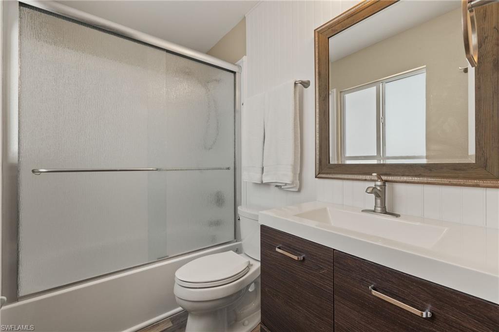Bathroom with shower / bath combination with glass door, vanity, and toilet